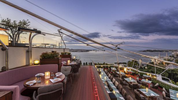 Ein Restaurant mit Tischen und Stühlen bietet einen Panoramablick auf das Meer bei Sonnenuntergang.