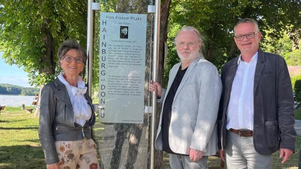 Michaela Gansterer-Zaminer, Jon Fosse und Bürgermeister Helmut Schmid stehen umgeben von Bäumen vor der Informationstafel zum "Jon Fosse Platz".