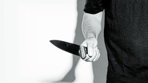 Man in black t-shirt, standing holding a knife.