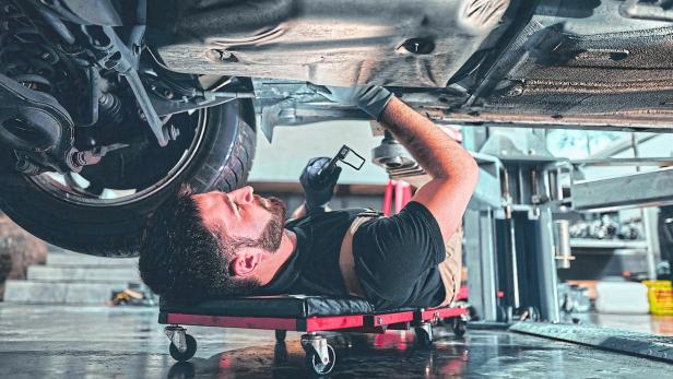 Male car mechanic worker working using wrench tool for repair, maintenance underneath car. Mechanic vehicle service checking under car in garage.