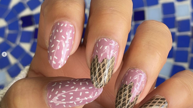 Eine Hand mit lackierten Nägeln im Eiscreme-Design vor blauem Mosaikhintergrund.