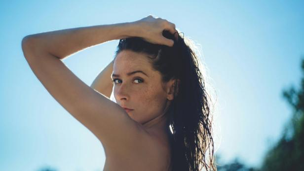 Eine Frau mit nassen, dunklen Haaren blickt über ihre Schulter in die Kamera.