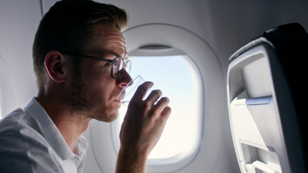 Mann sitzt im Flugzeug und trinkt Wasser