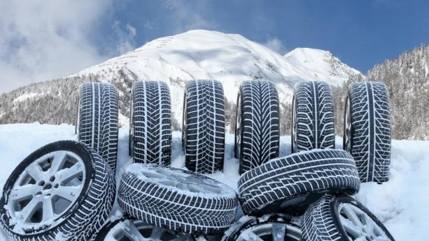 Mehrere Winterreifen liegen im Schnee vor einer verschneiten Berglandschaft.
