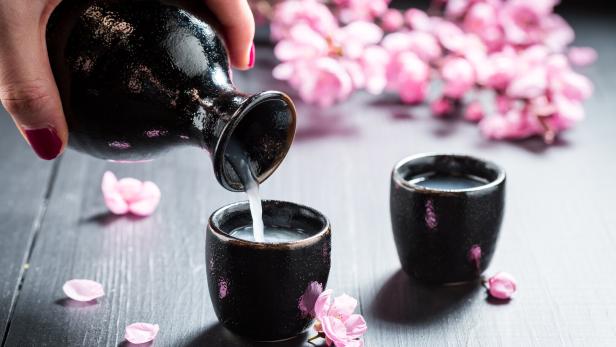 Sake wird in ein kleines Gefäß gegossen, im Hintergrund rosa Blüten.