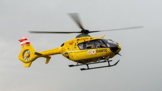 Ein gelber ÖAMTC Hubschrauber fliegt vor einem grauen Himmel.