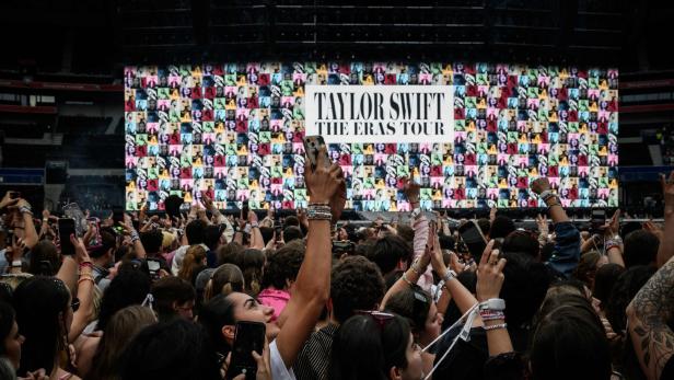 Fans stehen vor einer Leinwand, auf der Taylor Swifts "The Eras Tour" angekündigt wird
