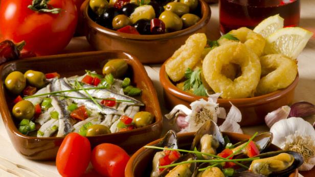 Verschiedene Tapas, darunter Oliven, Sardellen, Calamari und Muscheln, werden auf einem Tisch präsentiert.