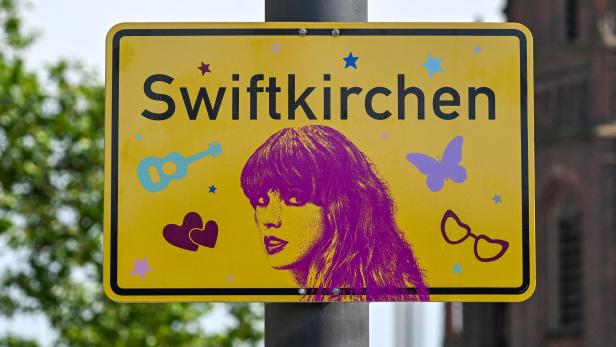 Ein deutsches Ortsschild, auf dem Swiftkirchen steht mit einem rosa Bild von Taylor Swift