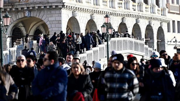 Viele Menschen überqueren eine steinerne Brücke mit Bögen und Laternen.