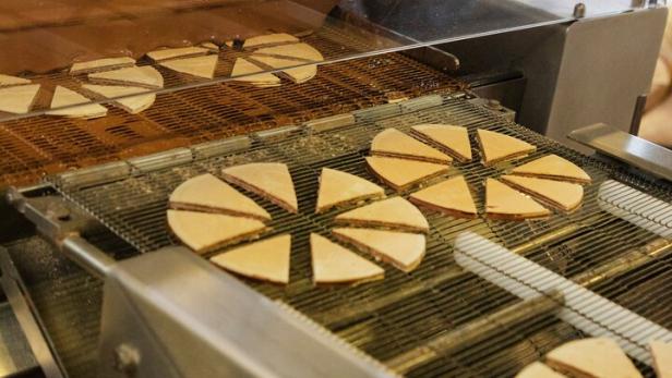 Eine Maschine überzieht Oblaten mit Schokolade.