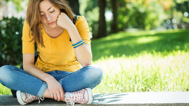 Ein trauriges Mädchen sitzt auf einer Mauer.