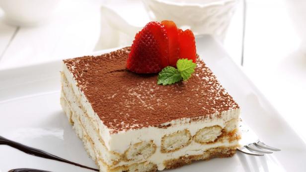 Ein Stück Tiramisu ist mit Erdbeeren und Schokoladensoße verziert.