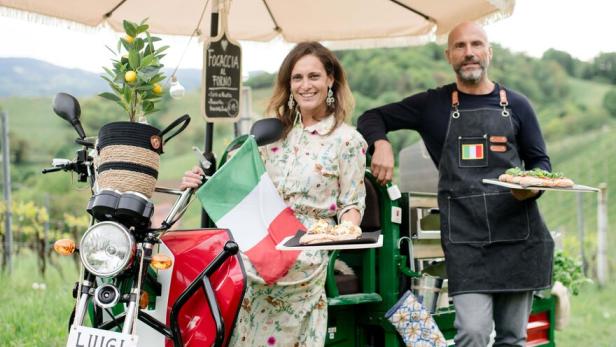 Eine Frau mit Italienischer Flagge und ein Mann mit Pizza stehen vor einem „Aperitivo“-Mobil.