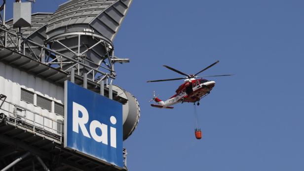 Large fire breaks out near Judicial City in Rome Ein roter und weißer Hubschrauber fliegt mit einem Wasserbehälter vor einem RAI-Gebäude.