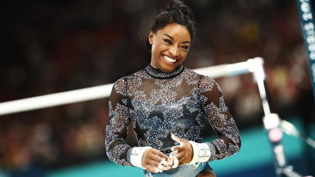 Simone Biles lächelt bei einem Gymnastikwettkampf.