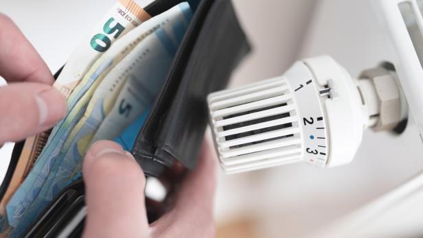 person holding wallet with cash next to turned down thermostat on radiator