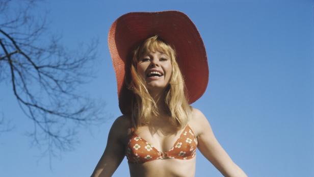 Eine Frau mit Hut und Bikini steht vor blauem Himmel.