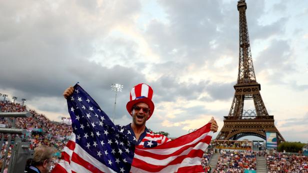 Ein Mann mit einer amerikanischen Flagge vor dem Eiffelturm