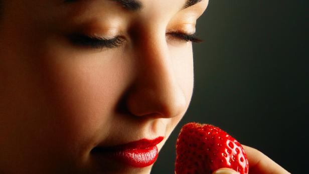 Eine Frau mit geschlossenen Augen hält eine rote Erdbeere in der Hand.