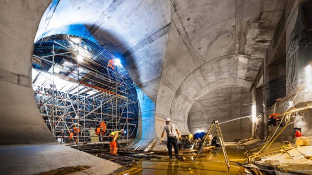 Bauarbeiter arbeiten im Inneren eines großen, im Bau befindlichen Betontunnels.