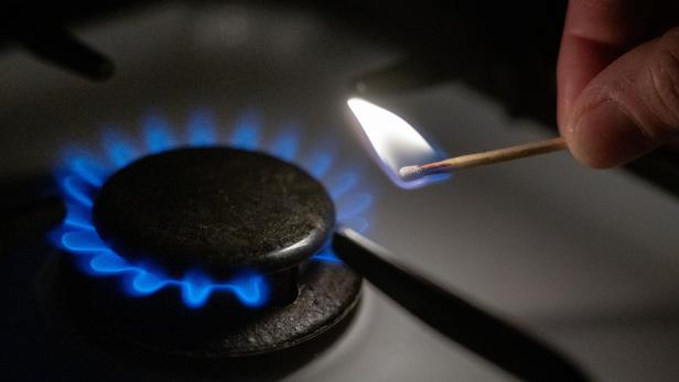 Ein Streichholz zündet eine blaue Gasflamme auf einem Herd an.