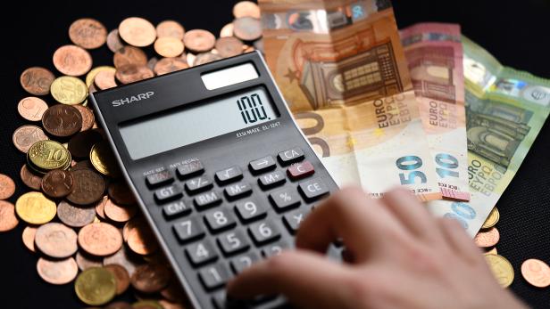 Eine Hand tippt auf einen Taschenrechner, daneben liegen Euro-Scheine und viele Münzen.