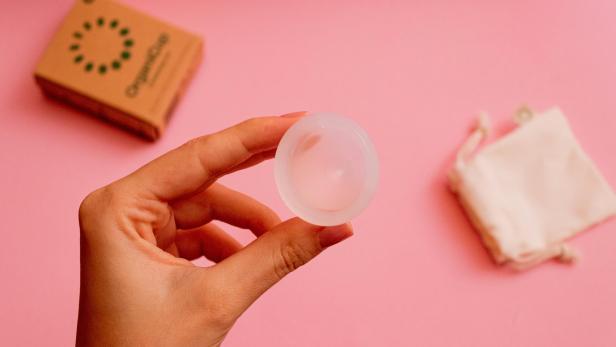 Eine Hand hält eine Menstruationstasse der Marke OrganiCup.