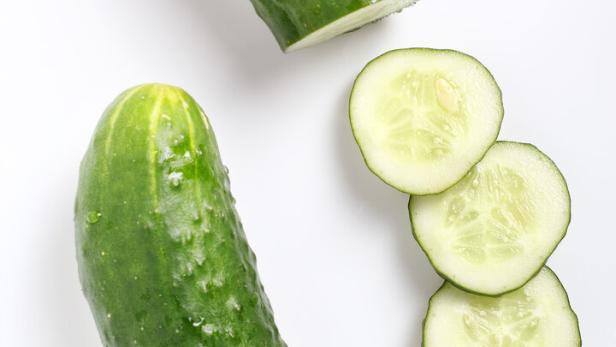 Ein ganzer und ein angeschnittener, grüner Salatgurke liegen auf einem weißen Untergrund.