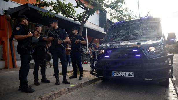 Mehrere spanische Polizisten stehen vor einem gepanzerten Polizeiwagen.