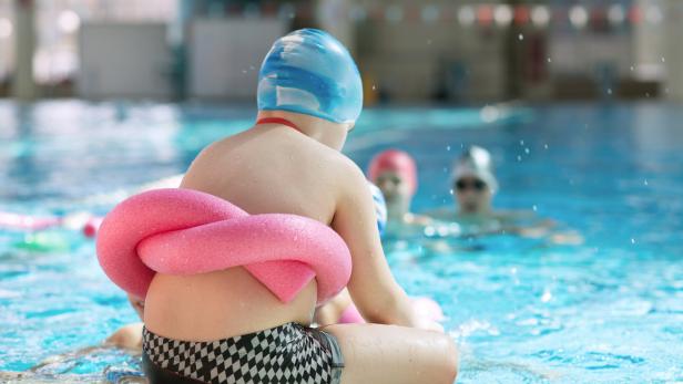 Ein Kind mit Übergewicht sitzt am Pool.