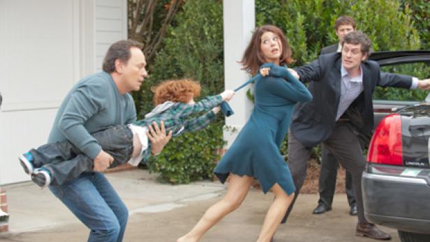 Ein Mann trägt ein Kind, während eine Frau an seinem Hemd zieht, um ihn zurückzuhalten.