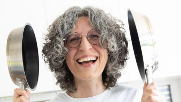 Elisabeth Koller hält lachend zwei Bratpfannen in die Höhe.