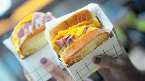 Zwei Egg-Drop-Toast-Sandwiches mit Käse und Speck werden in der Hand gehalten.