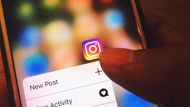 Ein Finger tippt auf das Instagram-Symbol auf einem Smartphone, es erscheinen Optionen wie „New Post“ und „View Activity“.