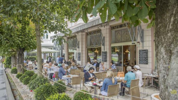 Gäste sitzen im Außenbereich des „Cafe Bazar“ unter schattigen Bäumen.