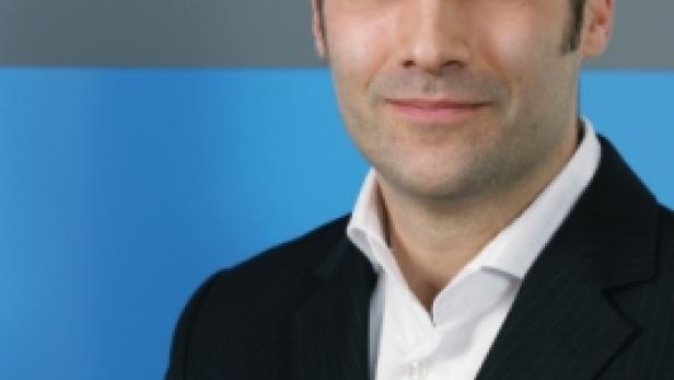 Ein Mann im Anzug vor einem blau-grauen Hintergrund.