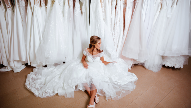 Eine Frau sitzt in einem Brautkleid vor einer Reihe von Hochzeitskleidern.