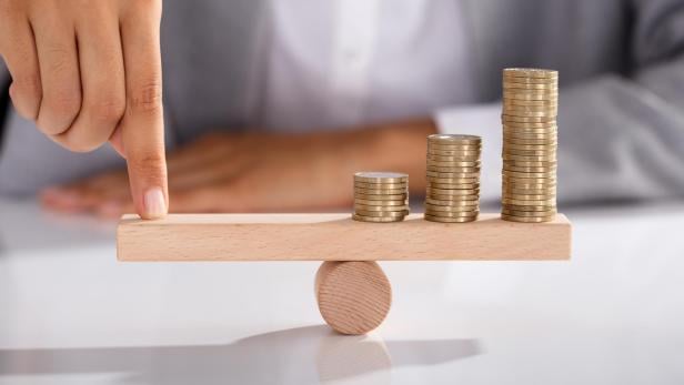 Businessperson Balancing Coins On Wooden Seesaw