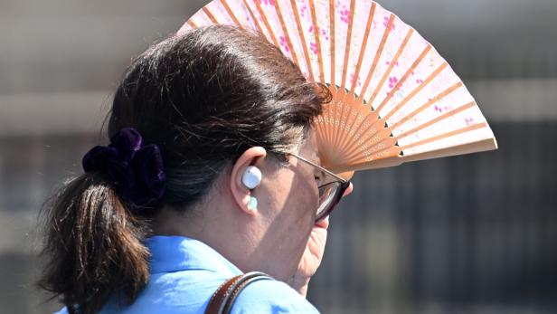 Sommerliche Hitze: Eine Frau schützt sich mit einem Fächer vor der Sonne.