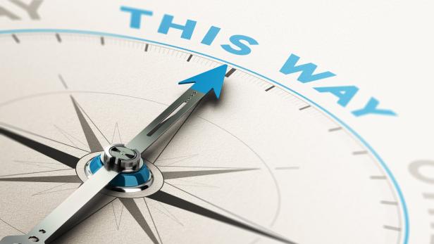 Ein Kompass mit einem blauen Pfeil zeigt auf die englischen Worte „THIS WAY“.