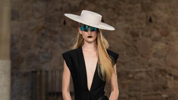Ein Model in einem schwarzen Hosenanzug, Hut und futuristischer Brille auf dem Laufsteg bei Louis Vuitton.