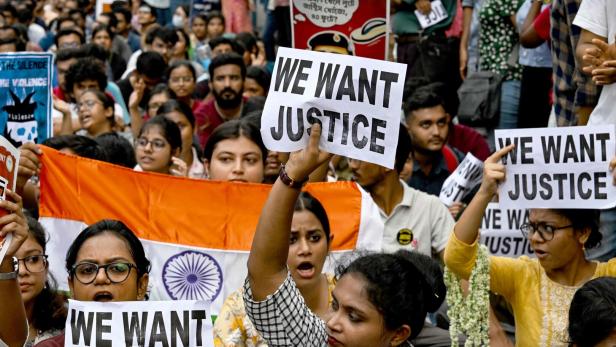 Eine Menschenmenge demonstriert mit der indischen Flagge und Schildern, die „We want justice“ fordern.