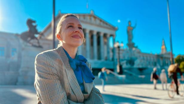 Nina Proll sitzt vor dem Parlament in Wien, von dem sie beeindruckt ist. Später darf sie auch auf der Regierungsbank Platz nehmen