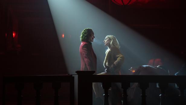 Der Joker im roten Anzug steht im Scheinwerferlicht mit Harley Quinn mitten in einem dunklen Gerichtssaal