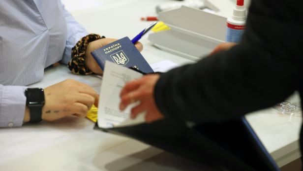 Eine Person reicht einen ukrainischen Reisepass an einem Schalter mit Formularen und Stempel weiter.