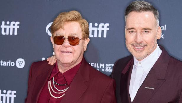 Elton John und David Furnish posieren gemeinsam vor einer Wand mit dem Logo des Toronto International Film Festival.
