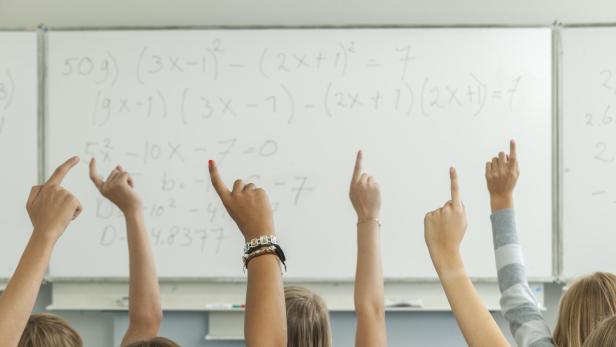 High school students in classroom raising hands