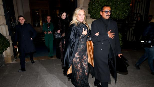 Kate Moss wird von einem Mann gestützt, während sie ein Gebäude verlässt.