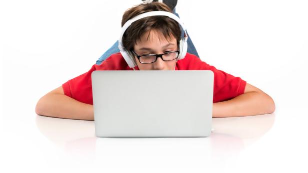 Ein Junge mit Brille und Kopfhörern liegt auf dem Boden und benutzt einen Laptop.